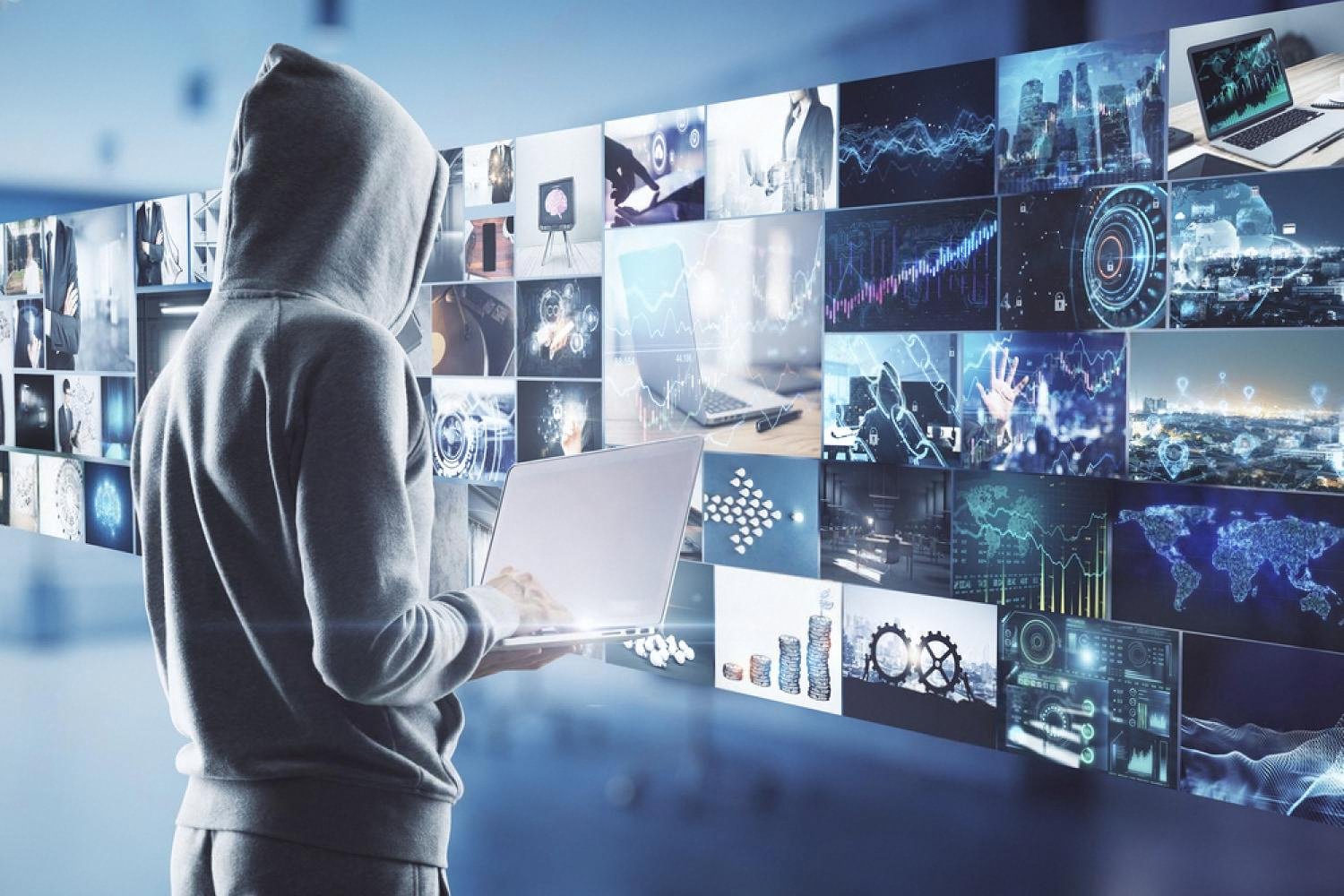 Person in a hoodie facing a wall of screens showing cloud data and analytics